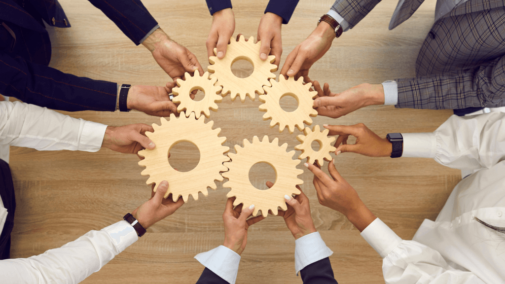 Image of business people working with outreached hands holding individual gears which, with the 7 leadership principles outlined by Tim Empringham, work together to drive an SMB's performance forward.