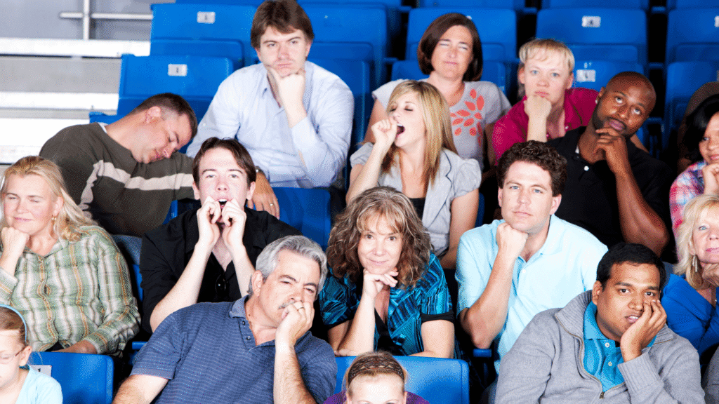 Image of a crowd that looks tuned out from the story that the presenter is telling. Various members of the crowd are napping, yawning, rolling their eyes, or looking very bored.