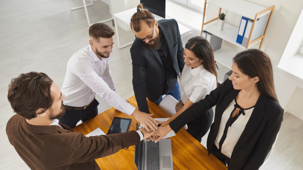 Picture of an SMB team who have their hands into the centre of their circle ready to raise them as a team with a "Go Team" chant signifying that anyone can lead regardless of position or title.
