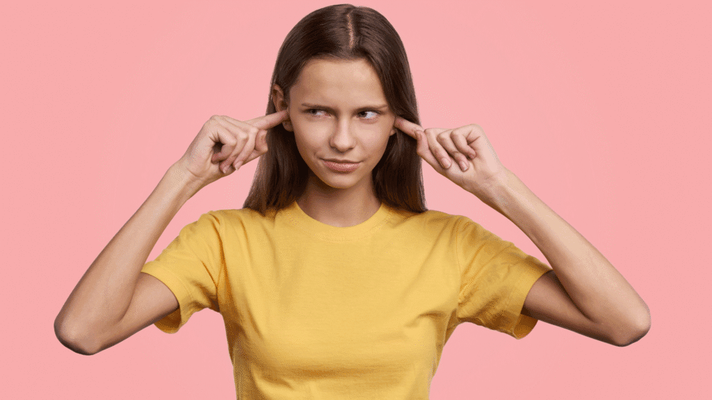 Picture of a woman with her ears plugged giving side eye to whoever is speaking off screen and ignoring the warnings.