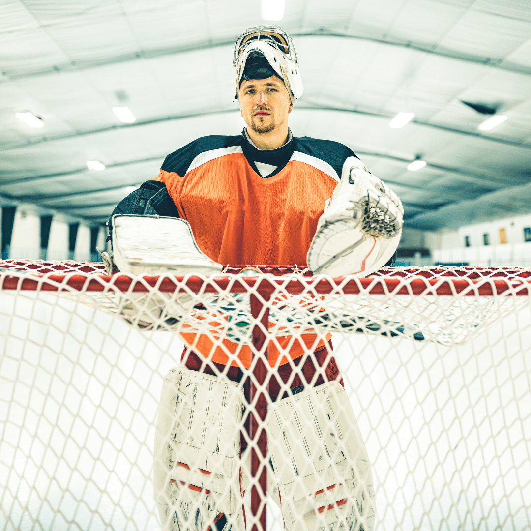 Picture of a hockey goalie standing at his net with his mask up, looking confident in. his abilities and preparation to "be" a goalie.