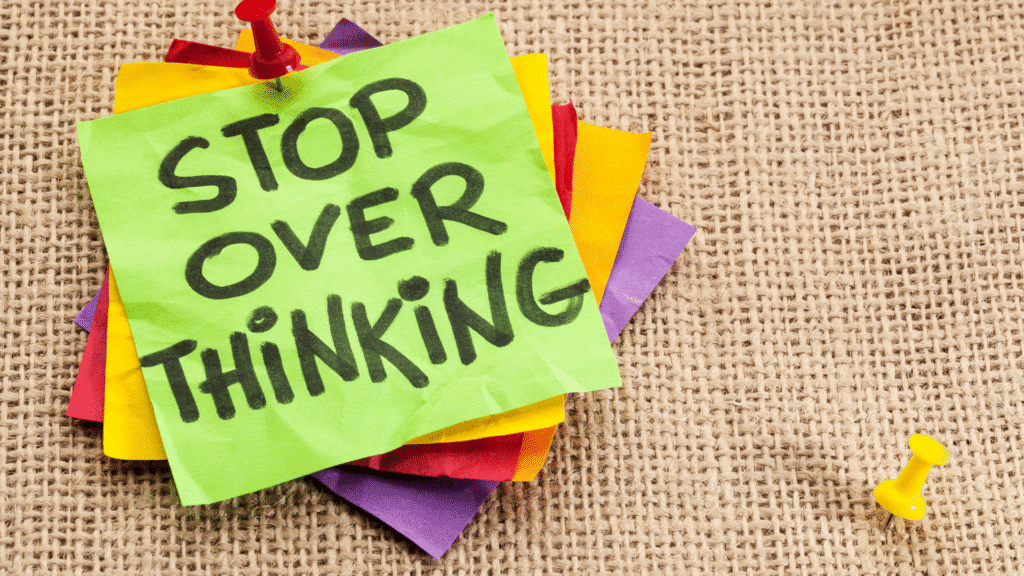 Picture of a stack of post-it notes tacked to a board with the top note reading "STOP OVER THINKING"