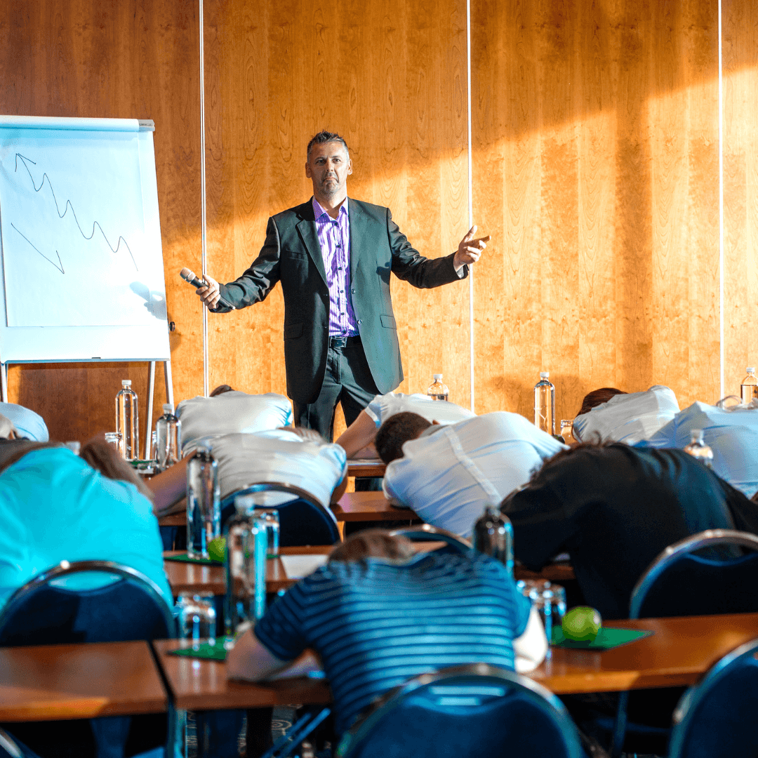 Picture of an SMB leader standing at the front of the meeting room in front of his presentation with all of the meeting attendees hunched over their desks and sleeping.