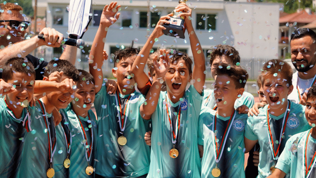 Picture of a team of kids who have won a trophy celebrating and holding up the trophy. The coach stands behind them proudly smiling and letting them have their moment.
