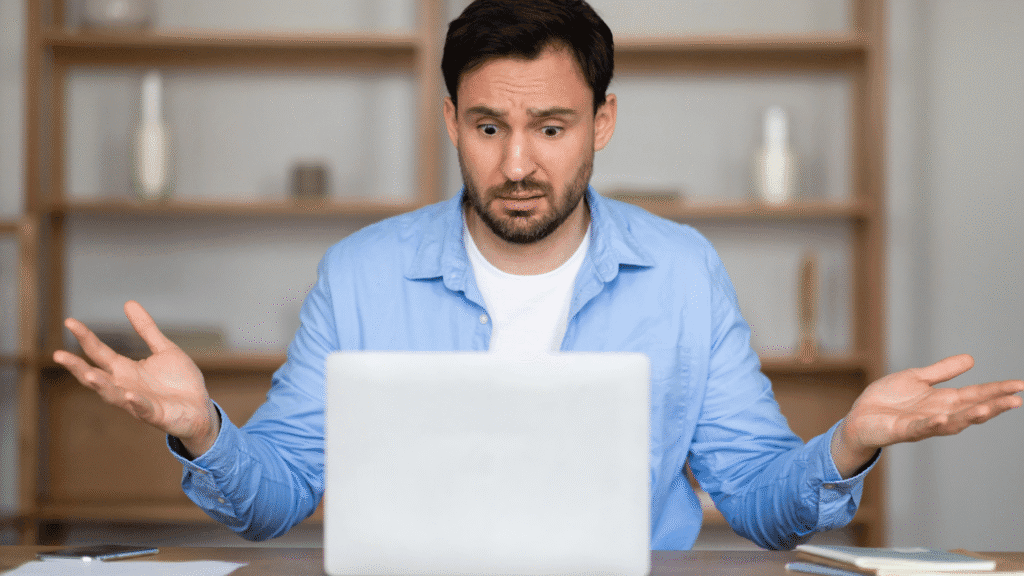 A man looking at his computer with confusion with his hands up in frustration as he reacts to a message he received in the way he interpreted it.